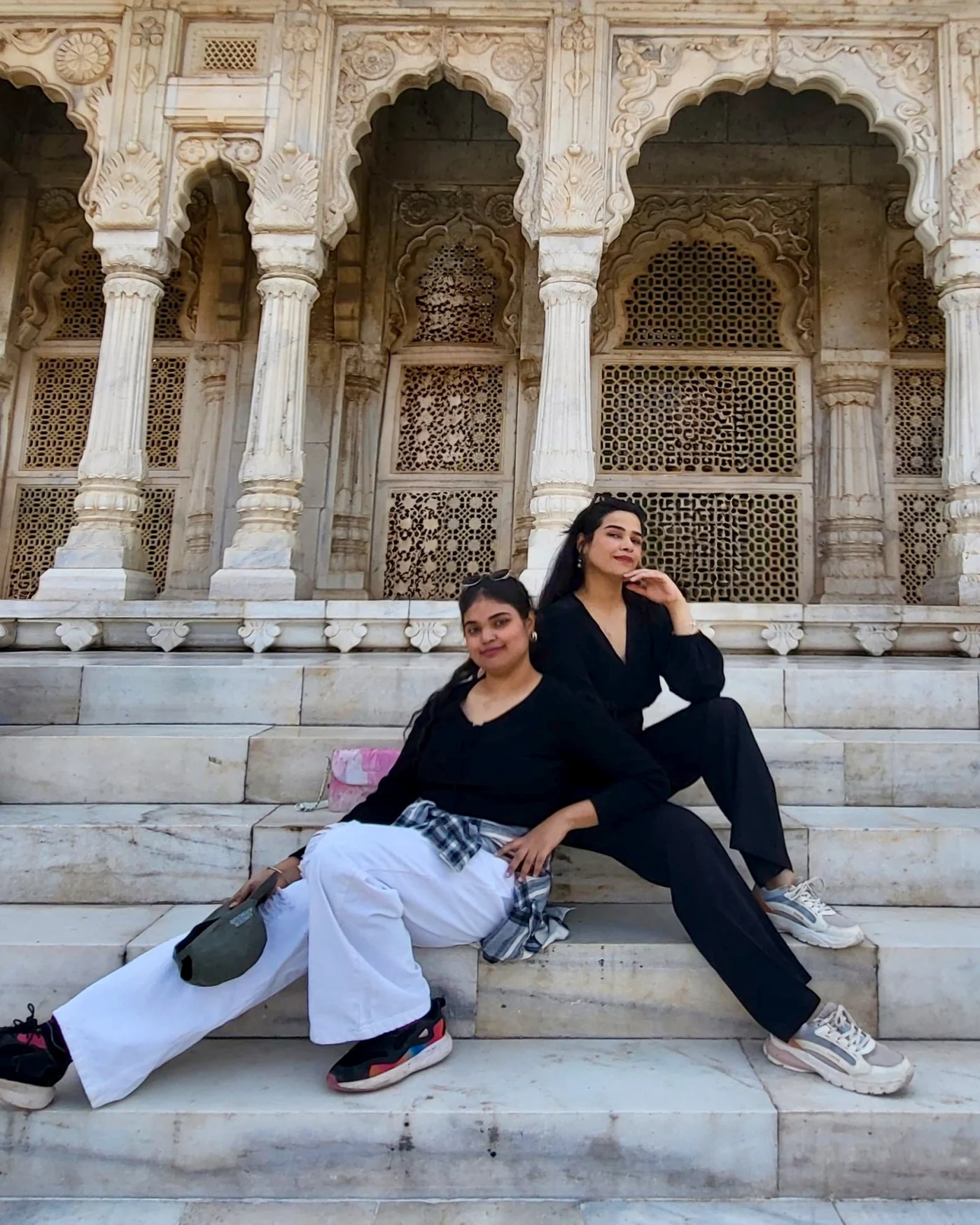 Hitanshi Watwani and Ashmeet Bharaj, the two artists behind Palette Pals, sitting on the marble steps of a carved Rajasthani monument